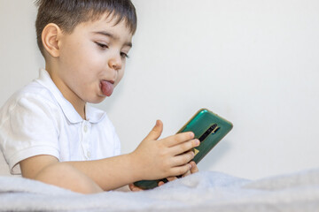 cute boy is speaking at the phone and making some funny faces. the kid is showing the tongue, or frowns or is too serious. speaking to parents, grandparents or followers. young little vlogger.