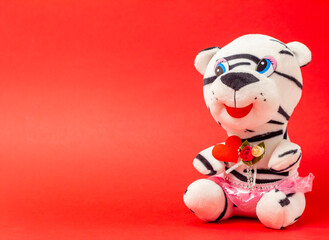white plush tiger with red heart on a red background with a place for the text, top view, Valentine's Day is the holiday of lovers.