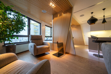 Luxury studio apartments in wooden colors with soft armchairs. Stylish modern kitchen area with bar counter and modern lamps