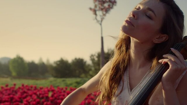 Inspired woman with cello making solo concert in beautiful spring park outdoors.