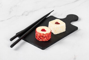Two creamy white chocolate mousse cakes with jelly hearts, in the form of round and square sweet sushi, sprinkled with small pieces of freeze-dried strawberries and coconut chips. Valentine's Day