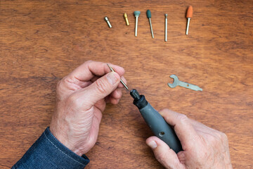 Overhead view of the hands of a craftsman preparing a rotary tool with an engraving accessory