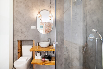 White porcelain sink with soaps on varnished pine countertop and gray Venetian stucco walls
