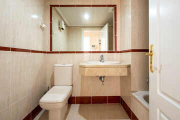 Toilet with cream porcelain sanitary ware, tiled walls with imitation marble tiles with red border and built-in mirror
