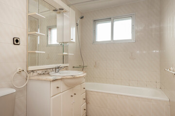 Conventional toilet tiled in white and cream with veined marble worktop and white cabinet with mirror