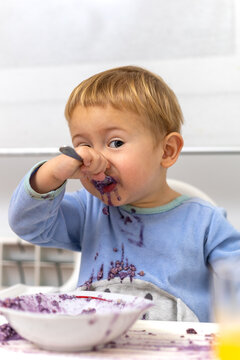 Ni&ntilde;o rubio con pijama azul empezando a mancharse la ropa desayunando