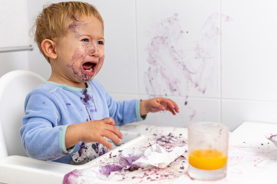 bebe llorando con la cara manchada en la trona despu&eacute;s de manchar toda la mesa y la pared con su comida