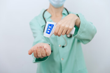 Temperature measurement gun in doctor hands. Close-up shot of doctor wearing protective surgical mask ready to use infrared isometric thermometer gun to check body temperature for virus symptoms