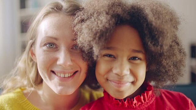 Cheerful Caucasian mother and black daughter smiling on cam, multiracial family