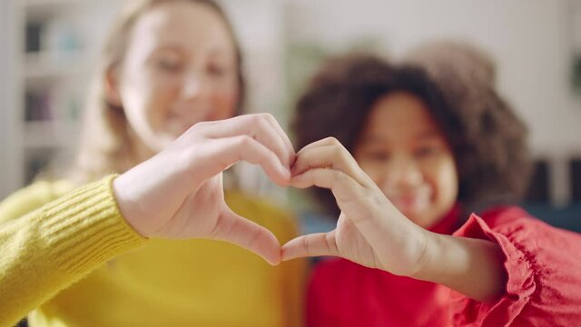 Caucasian mom and African American daughter making hand heart sign, adoption