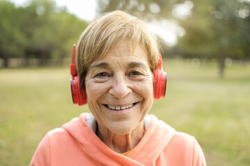 Senior woman listening playlist music outdoor at city park - Healthy elderly lifestyle