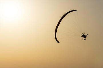 Paramotor vehicle tilted flying in a yellow sky by the sun