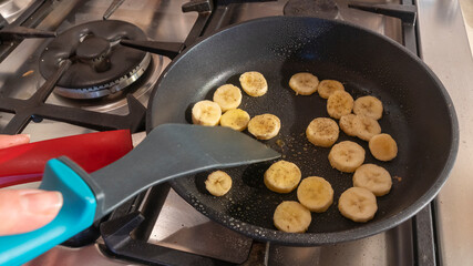 Top view of banana pieces with honey and cinnamon frying on kitchen pan. An exotic recipe for a sweet dish.