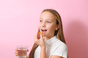 A teenage girl holds an omega 3 capsule in her hands on a colored background. 