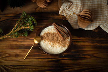 Scandinavian-style rice porridge. The rice pudding is in a blue ceramic bowl on a wooden table, with gingerbread cookies, cinnamon and dried orange slices.