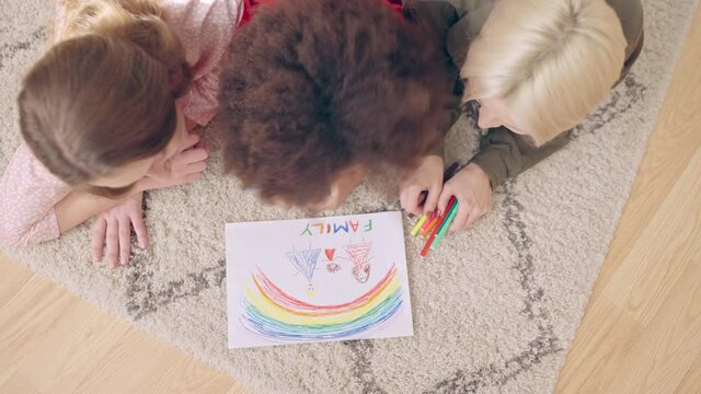 Top view of lesbian couple and little daughter drawing family picture on floor