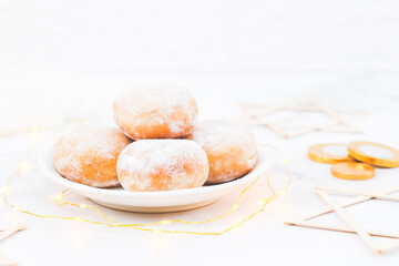 Donut with powdered sugar and cream in a saucer with a garland, coins and wooden Star of David