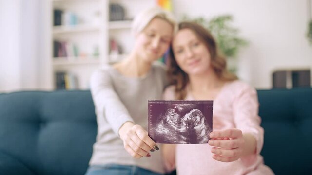 Pregnant lesbian couple showing ultrasound image on camera, expecting baby