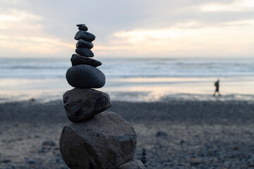 Zen stacking stones during sunset on the beach covered with rocks washed ashore at a low tide after Tonga's volcanic eruption.