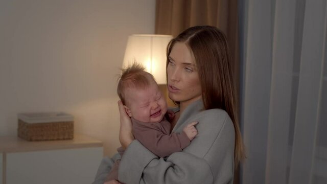 Worried Young Mother Holding Crying Newborn Baby In Arms, Comforting Upset Child