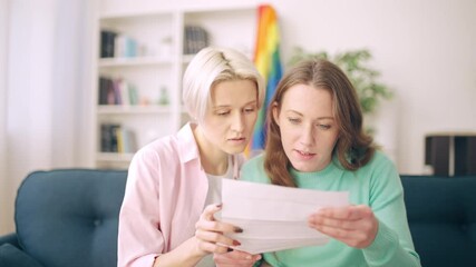 Nervous lesbian couple reading official letter together, upset with bad news