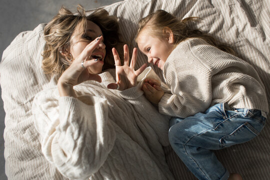 Mother and daugher in similar sweaters lying in bed and playing 