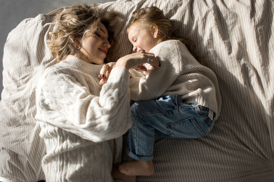 Mother and daugher in similar sweaters lying in bed and playing 