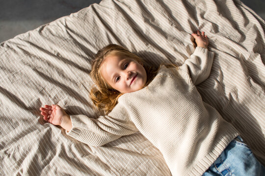 Little girl in cozy white sweater lying in bed
