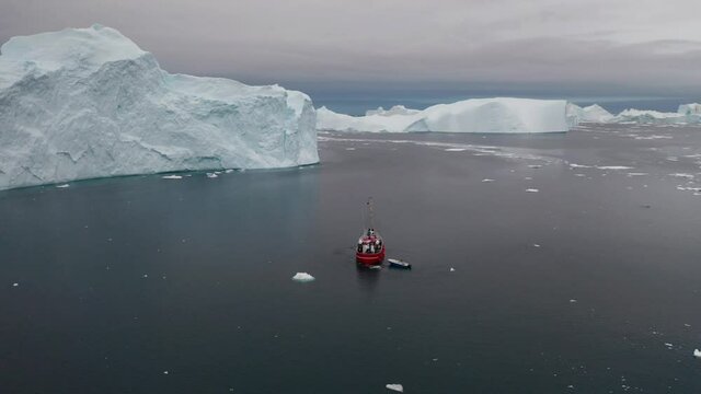 Red Boat Sailing In Front Of Big Icebergs From Aerial View