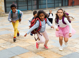 Portrait of cheerful tween boys and girls with school backpacks running in schoolyard in spring day.