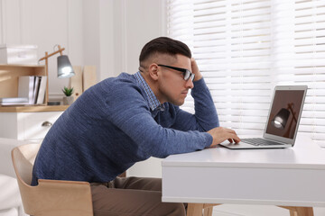 Man with poor posture using laptop at table indoors - obrazy, fototapety, plakaty