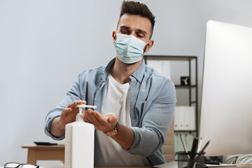 Fototapeta na wymiar Man applying hand sanitizer at workplace in office. Personal hygiene during Coronavirus pandemic