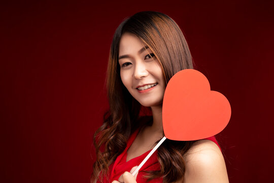 Valentine's Day. Smiling beauty girl long brown hair holding Valentine red hearts on red background.