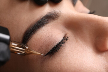Young woman undergoing procedure of permanent eye makeup in tattoo salon, closeup - obrazy, fototapety, plakaty
