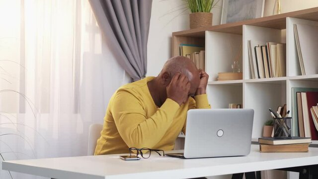 Boring video. Sleeping man. Bad feelings. Tired senior african guy falling asleep leaning head desk sitting with opened laptop light room interior.