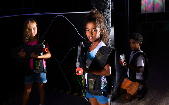 Portrait of nice african tweenager girl with laser pistol posing in laser tag labyrinth on background with her team