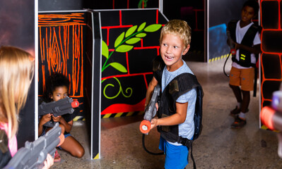 Portrait of positive tweenager boy with laser gun having fun on dark lasertag arena