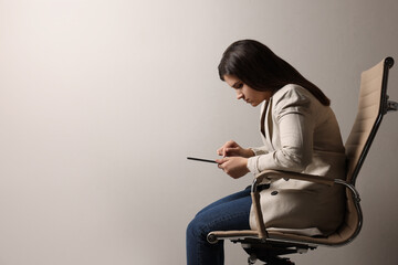 Young woman with bad posture using tablet while sitting on chair against grey background. Space for text - obrazy, fototapety, plakaty
