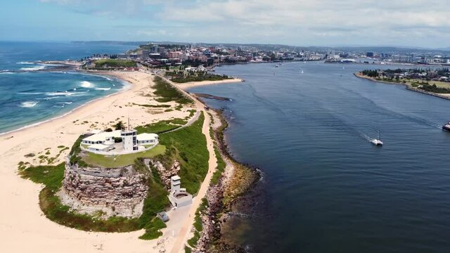 Aerial drone shot of Nobbys Beach lighthouse horseshoe Newcastle Harbour channel with boats yacht in inlet break wall NSW Australia 4K