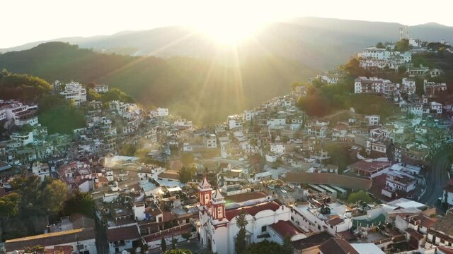 Aerial view of spanish colonial architecture in Taxo, Guerrero Mexico, old buildings in cityscape under morning sunlight, drone shot