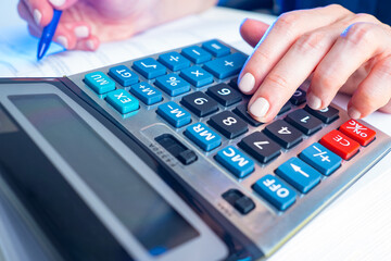 A woman uses a calculator. Calculations, accounting, statistics, analytics. A woman entrepreneur or accountant counts on a calculator. Calculator close-up. Calculation of profit and taxes in business.