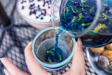 Hand pouring tea from glass teapot of butterfly pea Clitoria ternatea colorful color tea blue and...