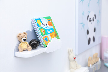 Small camera hidden between toy bear and book on shelf in baby room