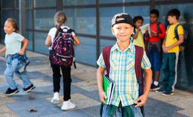 Portrait of smiling preteen schoolboy with workbooks in hands and rucksack on back in schoolyard. Back to school concept .