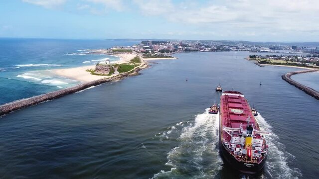 Aerial scenic drone shot of trade freight ship entering Newcastle Harbour Nobbys Beach Inlet Lighthouse trade tourism foreshore NSW Australia 4K