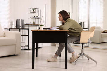 Young woman with bad posture working at table in office - obrazy, fototapety, plakaty