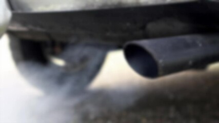 Slow motion and defocused shot combustion fumes coming out of car exhaust pipe which strongly of smoke. Poisonous carbon monoxide from vehicle on road, air pollution concept. Fume emissions traffic