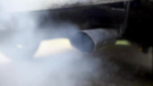 Defocused shot of combustion fumes coming out of car exhaust pipe which strongly of white smoke. Poisonous carbon monoxide from vehicle on road, air pollution concept. Fume emissions in the traffic
