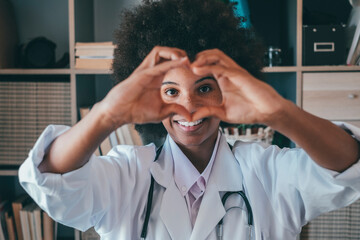 Woman doing heart shape gesture with hands. Smiling black female doctor making a love symbol using...
