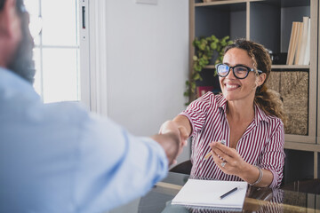Happy businesswoman shaking hand with male customer after deal or contract signing at office. Smiling saleswoman doing a handshake with client or job candidate at employment business meeting